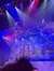 Two performers are balancing on a large, spinning apparatus under colorful stage lighting, with a snowy village backdrop.