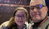 A man and a woman are smiling for a selfie with a blurred background that suggests they might be at an event or a venue with dim lighting.