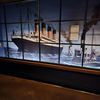 The image shows a large graphic panel of the RMS Titanic displayed across several window panes, with an epilogue plaque detailing historic information, likely part of an exhibition.