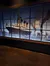 The image shows a large graphic panel of the RMS Titanic displayed across several window panes, with an epilogue plaque detailing historic information, likely part of an exhibition.