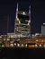 The image features a night view of a brightly lit, distinctive high-rise building in an urban setting, juxtaposed with older, historic architecture in the foreground.