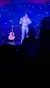 A performer in an Elvis Presley-inspired costume is singing on stage in front of an audience under blue stage lights.