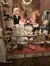 The image shows a vintage-style display with mannequins dressed in historical clothing, antique furniture, and decorative items giving the impression of a period scene behind a glass barrier.