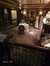 This image depicts a vintage style room with ornate furnishings, a set dining table for two, decorative mannequins dressed in historical attire, and richly patterned rugs, evoking an old-world ambiance.