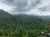 The image shows a lush, forest-covered mountainous landscape under an overcast sky, with a tall building rising distinctly among the trees.