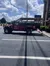 The image shows a red, modified Jeep with an open roof structure, designed for tours, parked in a lot on a sunny day with a digital billboard in the background that reads 