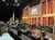 The image shows an interior view of the Grand Ole Opry stage, equipped with musical instruments, with people sitting and a large Opry logo displayed prominently in the background.
