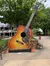 The image features a giant guitar sculpture with ornate detailing, placed as a landmark in front of a building with some park benches nearby.