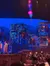 The image showcases a colorful theater set with a Middle Eastern theme, vibrant hanging lanterns, and an audience waiting in anticipation for a performance to begin.