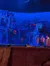 The image shows a theater stage set up to resemble an exotic, stylized town bathed in blue light, likely before or during a performance.