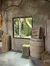 The image shows an indoor setting with a stone-like wall and a large window revealing a green, plant-filled enclosure, accompanied by wooden crates and a barrel, creating a rustic or warehouse-like atmosphere.