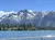 The image showcases a breathtaking view of a snow-capped mountain towering over a forest and a sparkling blue lake, all under a clear sky.