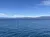 The image shows a serene blue lake with a mountain range in the background under a clear sky with scattered clouds.