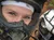 Two people wearing helmets are taking a selfie while riding an all-terrain vehicle (ATV) on a muddy trail.