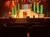 Four performers are singing on a brightly lit stage with dynamic lighting and a vibrant backdrop, as seen from the audience perspective.