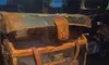 The image shows an aged and weathered leather trunk on display, possibly an artifact belonging to a passenger from the Titanic, as indicated by a placard in front of it.