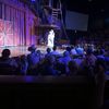 Audience members watch a performer in a cowboy costume on stage at what appears to be a western-themed theater.