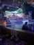 The image shows a themed restaurant with patrons seated at tables, watching performers on a mock wooded riverside set with a waterfall in the background.