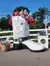 A large decorative cowboy boot filled with patriotic flowers stands prominently beside a fence under a clear blue sky.