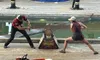 Two competitors clad in plaid shirts simulate a sawing competition during a lumberjack-themed performance.