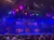 The image shows a vibrant theater stage with a colorful, ornate set design and hanging lanterns, with an audience in the foreground possibly waiting for a performance to begin.