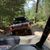 The image shows a view from inside an off-road vehicle following another off-roader through a forest trail.