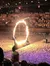 The image captures a performer on horseback jumping through a large ring of fire in front of an audience.