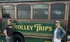 A man and a woman are standing next to a green trolley bus that bears the sign