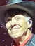 A performer in a cowboy hat and decorated suit is on stage under colorful stage lights, with a smile and an extended hand, suggesting an engaging moment with the audience.