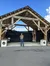 A man stands smiling in front of a rustic wooden pavilion adorned with star motifs under a blue sky with white clouds.