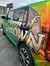 The image shows a car with a colorful, reflective wrap featuring the text