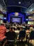 An audience is seated at tables in a theater with their attention directed towards a brightly lit stage framed by a decorative arch with the words