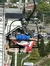 A person is seated on a ski lift chair adorned with a Texas flag, overlooking a street and greenery in a hilly area.