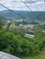 An empty chairlift seat hovers above lush greenery with a view of a town built within a valley of rolling hills in the background.
