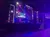 The image shows a stage with modern lighting and video screens prepared for an event, featuring vertical banners with the letter 'R' illuminated on each.