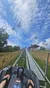 The image captures a person's point of view while seated in an alpine coaster, descending a metal track with chairlifts overhead against a blue sky with scattered clouds.