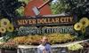 A child is standing in front of the Silver Dollar City sign, adorned with giant sunflowers and an ax, during the Ozark Mountain Summer Celebration.