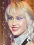 A figure, likely a wax figure, resembling a woman with blonde hair in a black dress, poses confidently in front of glittering multicolored curtains with sparkling light reflections on the floor.