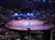 The image shows a large indoor arena with a performance featuring horses and performers in costumes, surrounded by an audience seated in tiers.