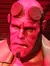 This image shows a life-sized model of a red-skinned, muscular, comic book character with a distinctive hand and circular patterns on his forehead, standing against a red and shadowed backdrop.