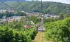 Passengers ride a chairlift above lush greenery with a panoramic view of a town nestled in a valley below.