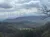 The image showcases a scenic view of a rolling mountainous landscape, with a patchwork of fields and trees under a sky filled with large, billowing clouds.