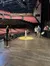 The image shows a view from a stage looking out into an empty theater auditorium with red seats and a few people standing on the stage, including one near a microphone stand.