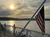 The image captures a serene sunset over a body of water with a gently waving American flag in the foreground, framed by an ornate white railing.