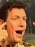 A person is standing in front of a background depicting a golf course, wearing a Boston Bruins hockey jersey, and making a comical gesture with their hands pulling down on their face to stretch their eyes wide open.
