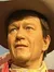 A wax figure of a cowboy, complete with a hat, bandana, and rifle, stands against a backdrop of a desert scene with a cactus.