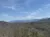 The image shows a scenic view of a mountain range with a clear blue sky and sparsely distributed houses nestled among leafless trees.