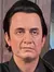 A man is posing with his arm around a lifelike wax figure of a seated guitarist at a Madame Tussauds exhibit.