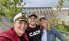 Three smiling people take a selfie in front of a large dam.