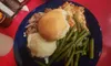 The image shows a hearty meal consisting of shredded meat on a bun, mashed potatoes, green beans, and gravy, served on a blue plate with a bottle of ketchup and a container of dressing on the side, all set on a red table.